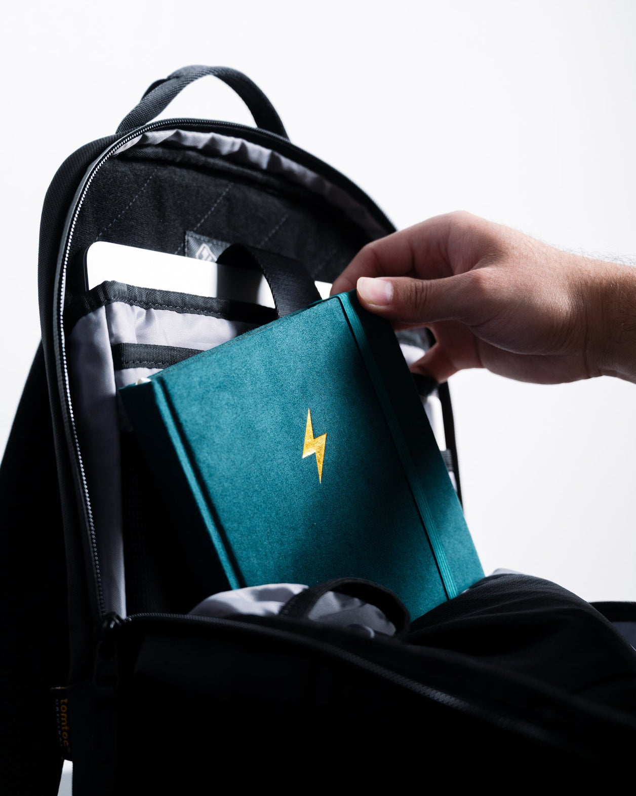 Person placing a teal book with a yellow lightning bolt on a black backpack.