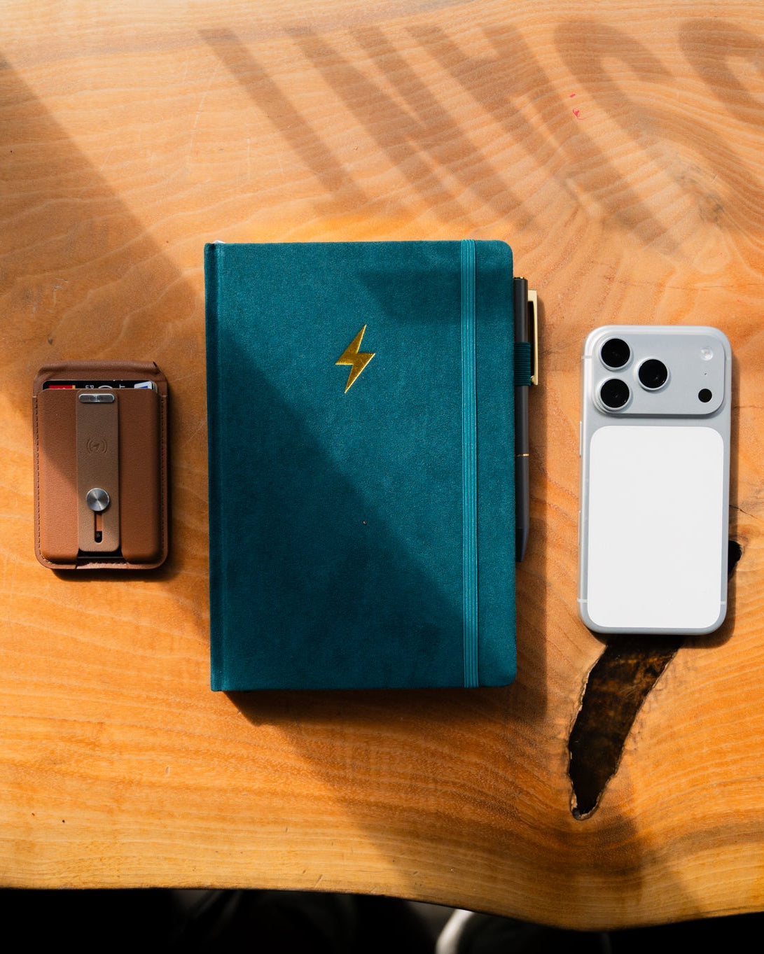 Teal wallet with lightning bolt design on a wooden surface with a smartphone and metallic wallet.